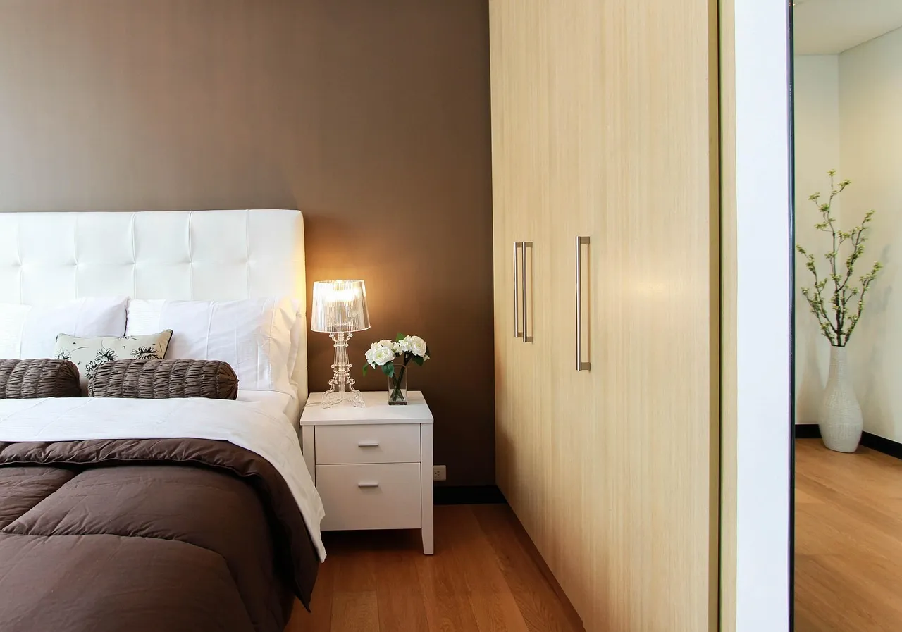 A calm bedroom in warm lamplight, bed made and nightstand clear — the environment better sleep starts in