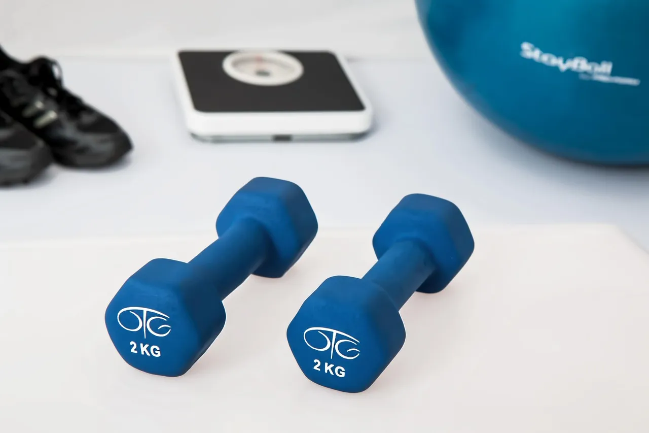 A pair of light dumbbells beside a bathroom scale and exercise ball — strength training starts at home scale